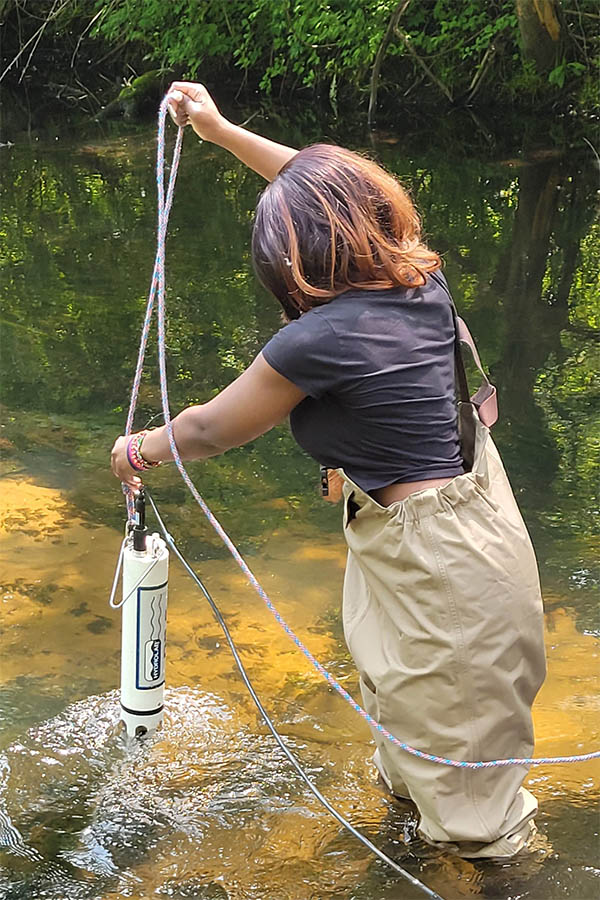 Student in waders standing in a stream deploying they Hydrolab data sonde.