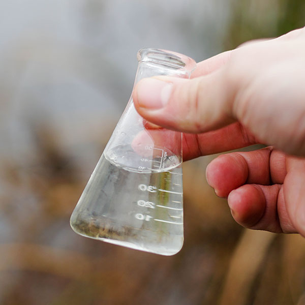 Hand holding a chemical flask with river water.