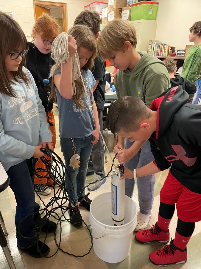A group of five students submerging the Hydrolab data sonde into a bucket of water.