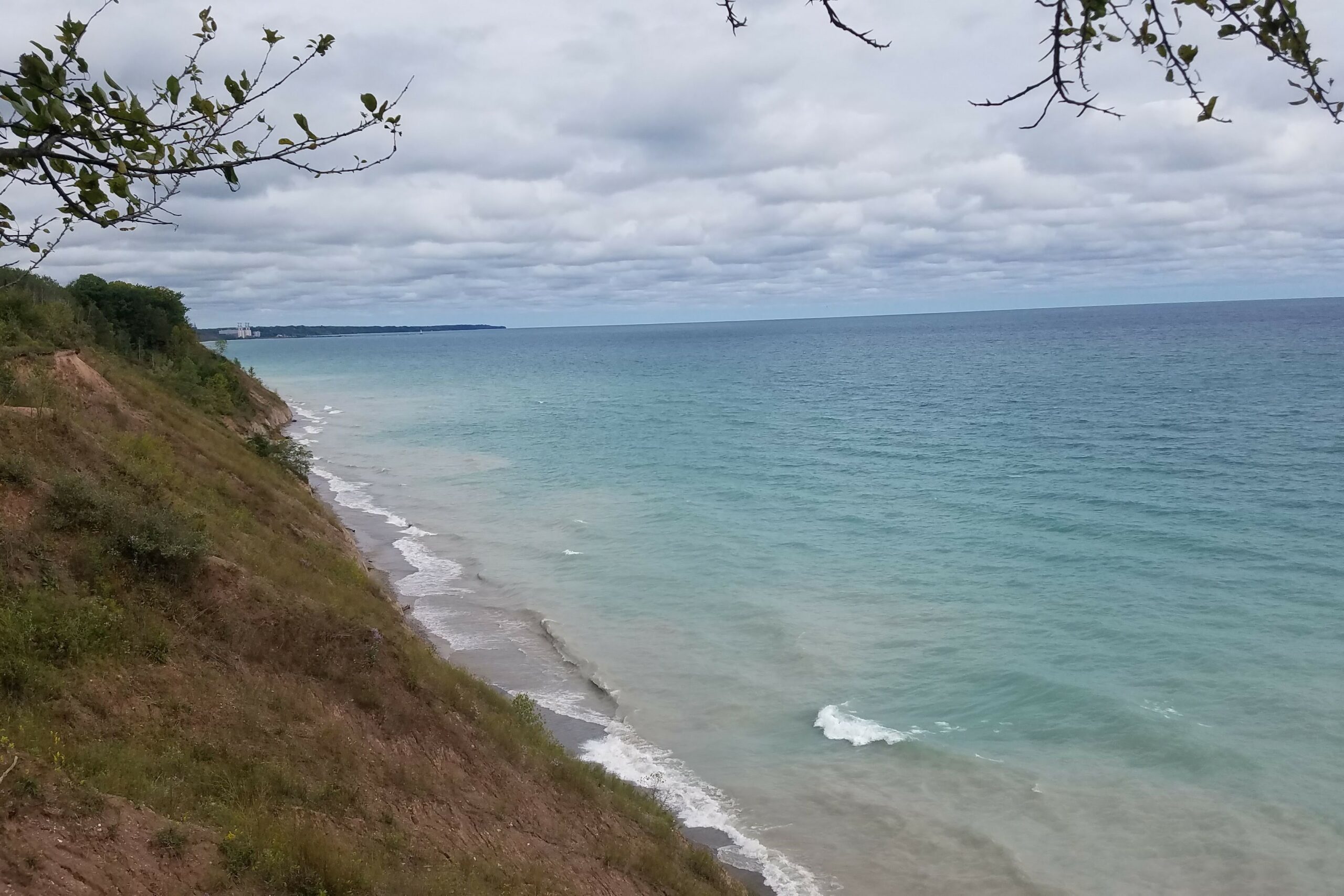 Image of a steep coastal embankment where sand and soil are washing into the lake creating cloudy water along the coastline.
